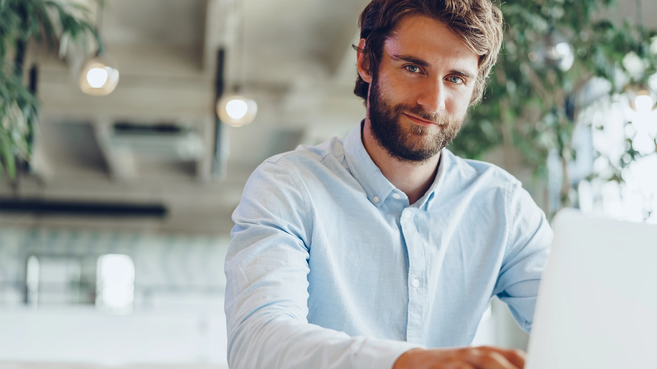 Mann im hellblauen Hemd am Laptop im modernen Büro mit Pflanzen – digitales Arbeiten.