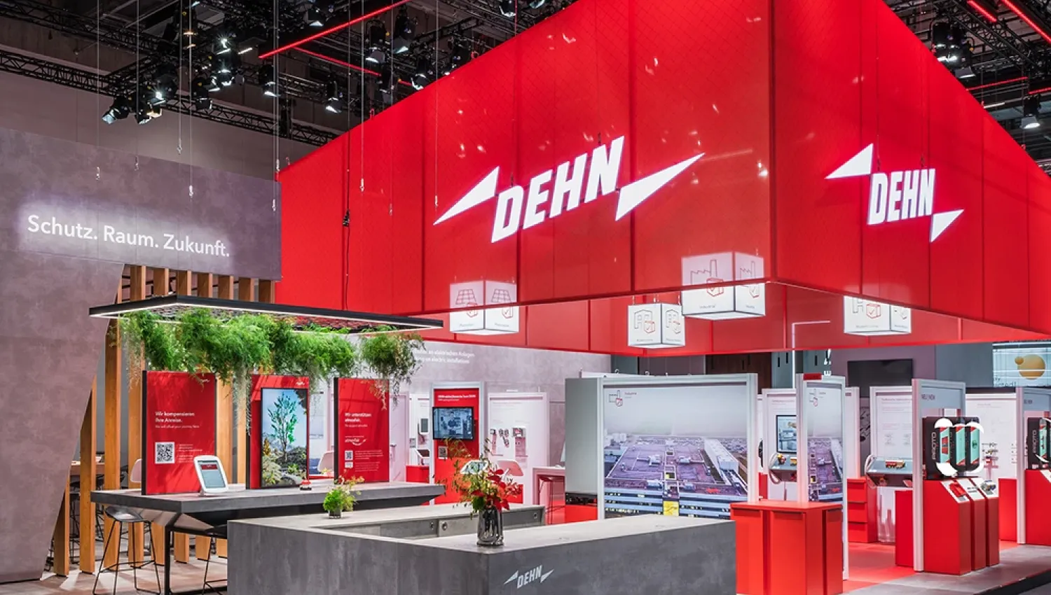Trade fair booth with large red DEHN cube, illuminated logo, exhibition counters, displays, and visible text “Schutz. Raum. Zukunft.”